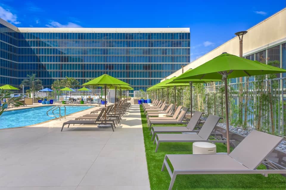 Rooftop pool area with lime green umbrellas, lounge chairs, modern building, and blue sky