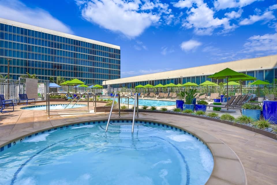 Resort pool deck with hot tub, lime green umbrellas, and high-rise hotel building backdrop