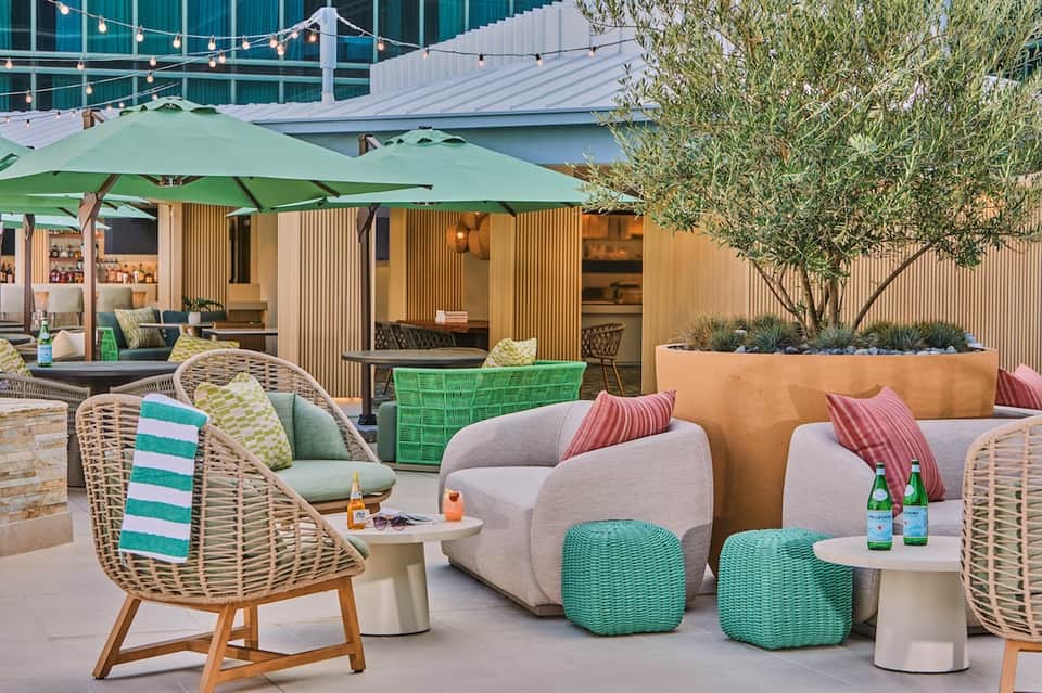 Modern outdoor lounge with woven chairs, green umbrellas, string lights, and contemporary furniture