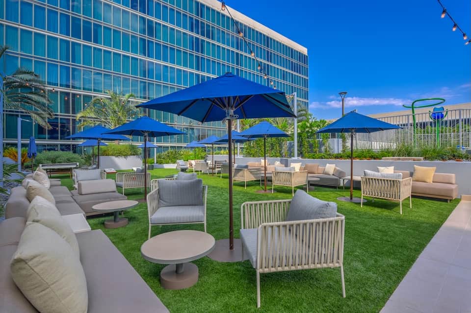 Rooftop terrace with blue umbrellas, lounge furniture, artificial grass, and city skyline