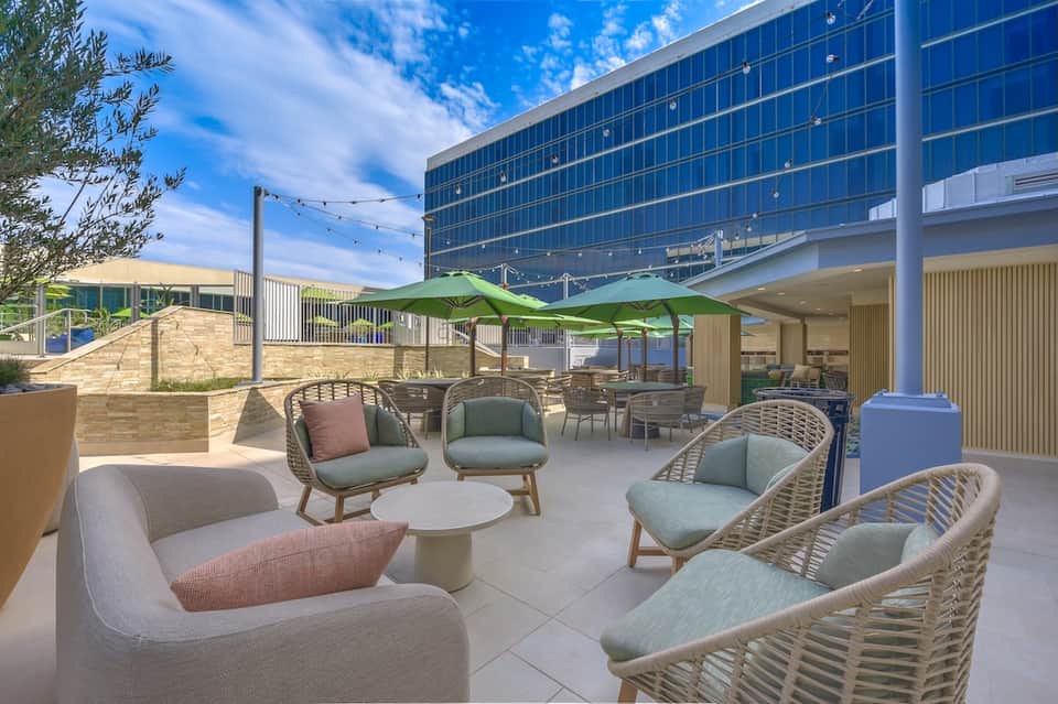 Modern outdoor lounge area with woven chairs, green umbrellas, and contemporary resort building