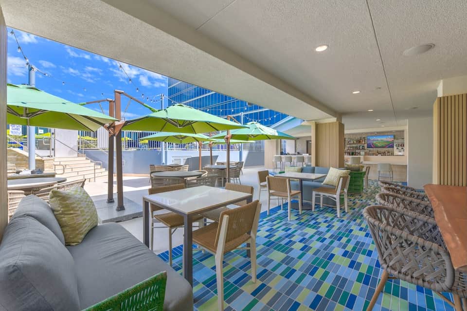 Modern lounge area with lime green umbrellas, white furniture, blue mosaic tile floor, and indoor-outdoor design