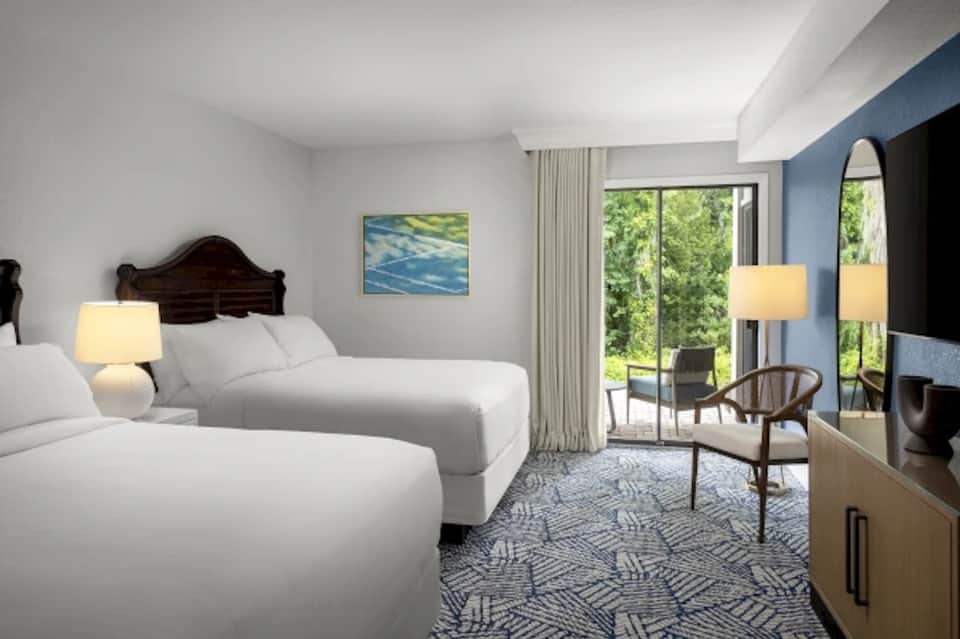 Hotel guest room with two beds, blue accent wall, balcony access, elegant furnishings, and modern decor
