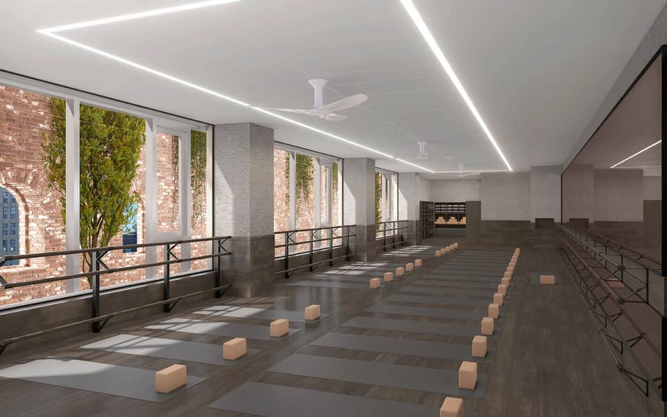 Modern yoga studio with floor mats, green plant walls, floor-to-ceiling windows, and contemporary lighting