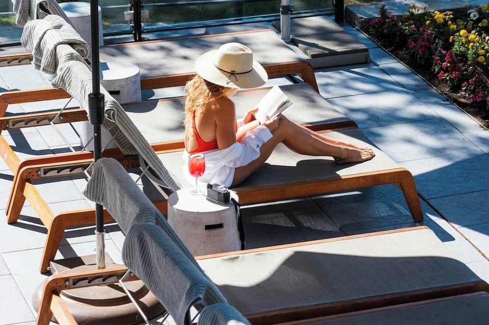 Woman lounging on padded deck chair with cocktail, ocean views, and flowering garden backdrop