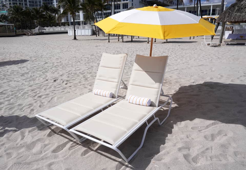 Beach loungers with cream cushions and yellow and white umbrella on sandy beach near resort