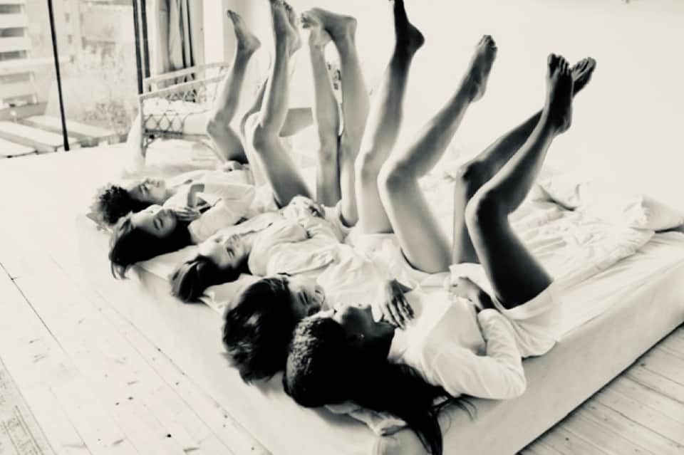 Black and white photo of women lying on bed with legs up in playful pose