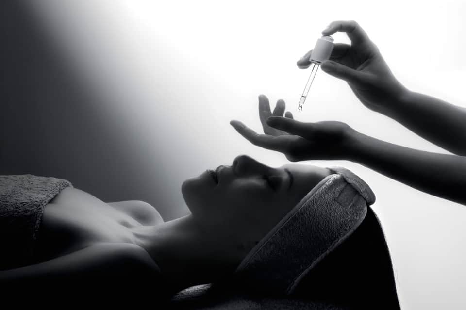Silhouetted hands applying facial serum or treatment to woman's face