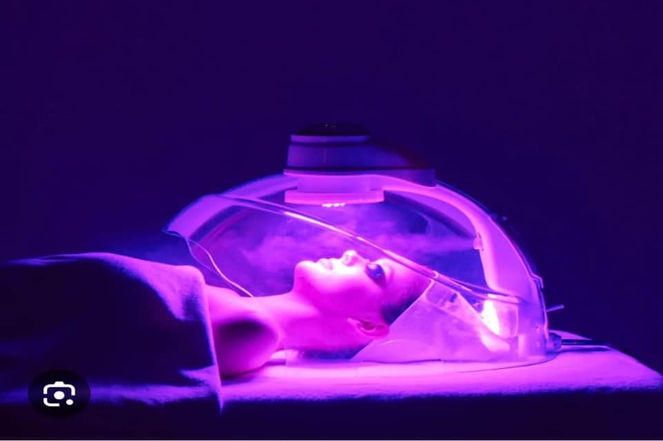Woman in UV light spa pod receiving light therapy beauty treatment