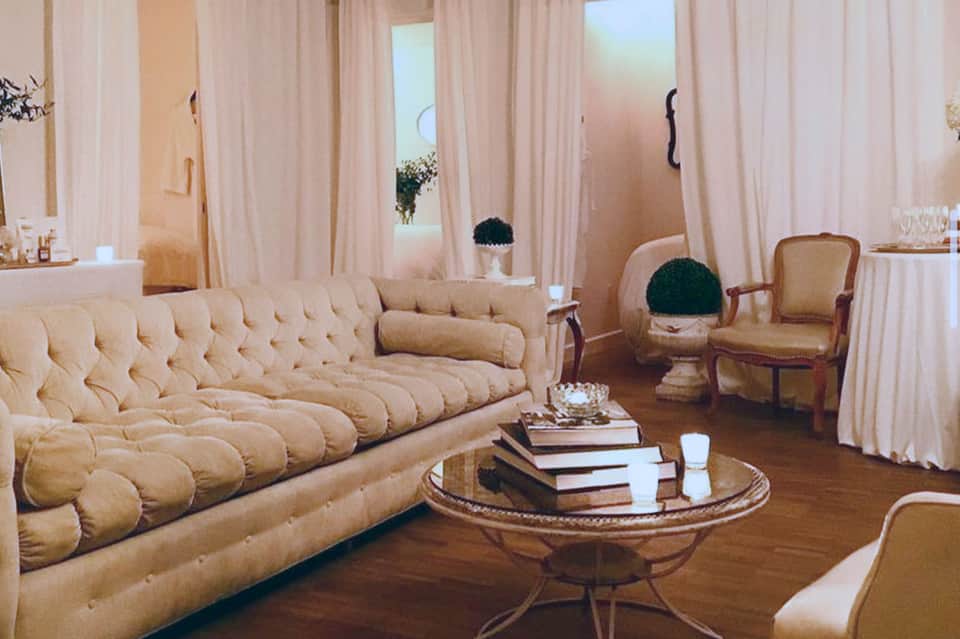 Luxury spa lounge with quilted beige sofa, cream armchairs, floor-to-ceiling windows, and warm lighting