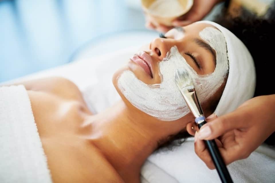 Client receiving facial mask application with brush by spa professional during treatment