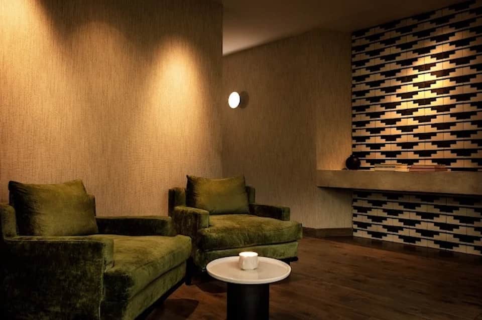 Modern spa lounge with olive green velvet armchairs, textured wall panels, and ambient lighting
