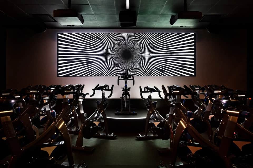 Upscale spin class studio with stationary bikes facing hypnotic geometric wall display