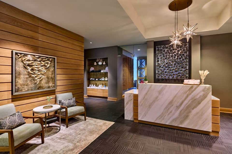 Modern hotel reception area with marble counter, wood paneling, and contemporary chandelier