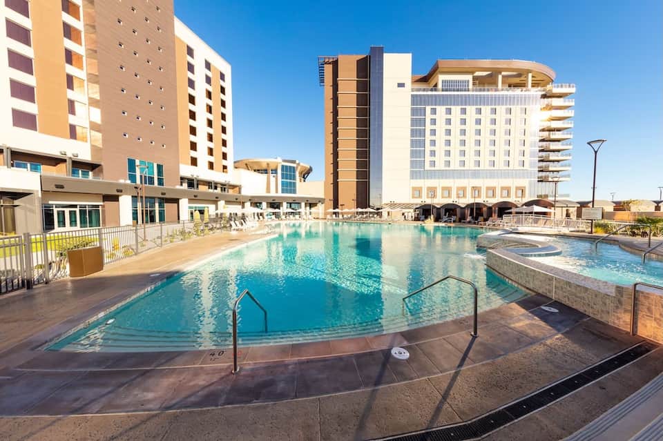 Resort pool complex with turquoise water, multi-story hotel building, dome cabanas, and spa area under blue sky