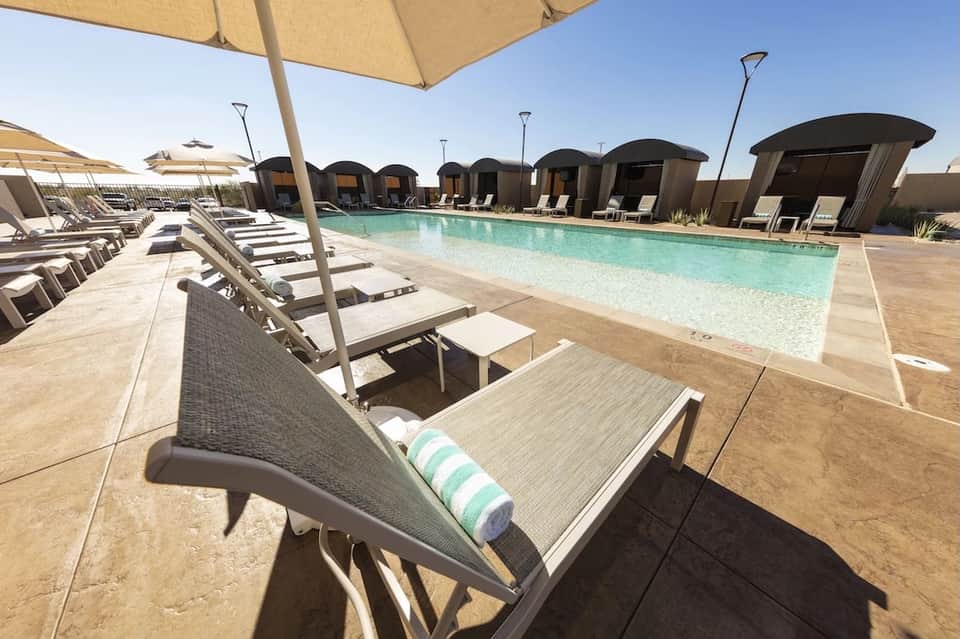 Poolside loungers with tan umbrellas and striped cushions, dome cabanas in distance across expansive deck