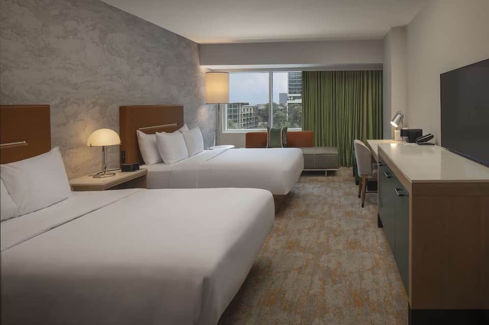 Modern hotel bedroom with two queen beds, work desk, and floor-to-ceiling windows with city views