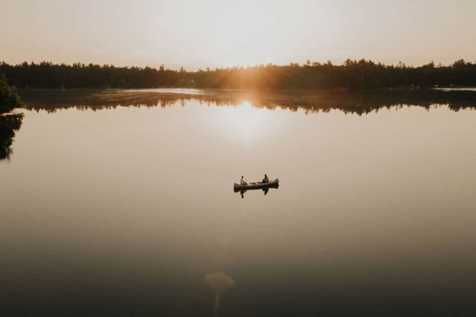 Two people in canoe on mirror-still lake at golden hour sunrise