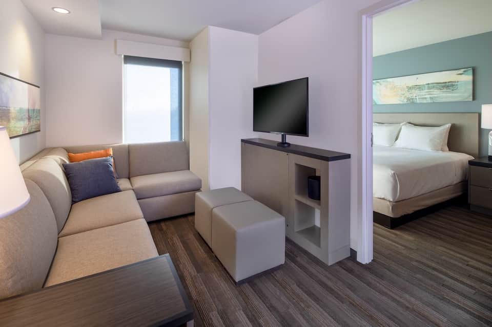 Suite interior with living area sofa, TV, bedroom with queen bed, and modern furnishings