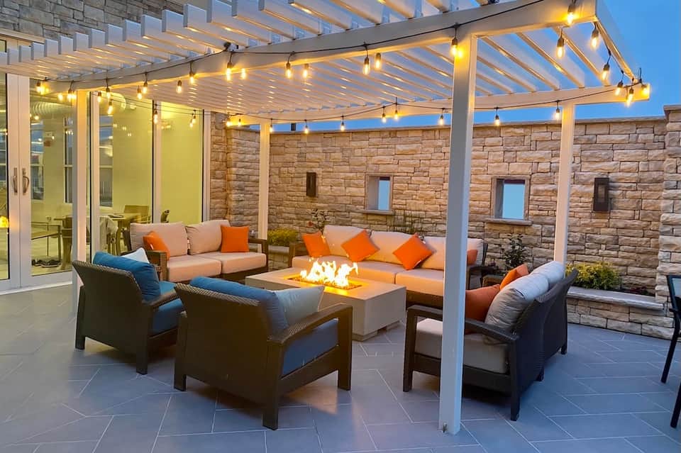 Illuminated patio pergola with fireplace, comfortable seating, and ambient lighting