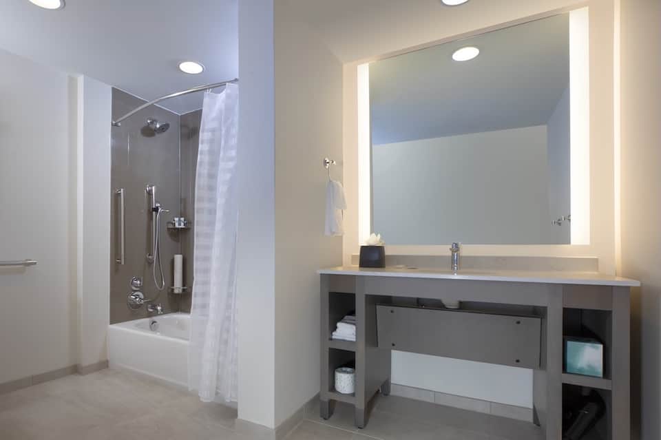 Modern bathroom vanity with illuminated mirror, storage cabinets, and adjacent shower enclosure
