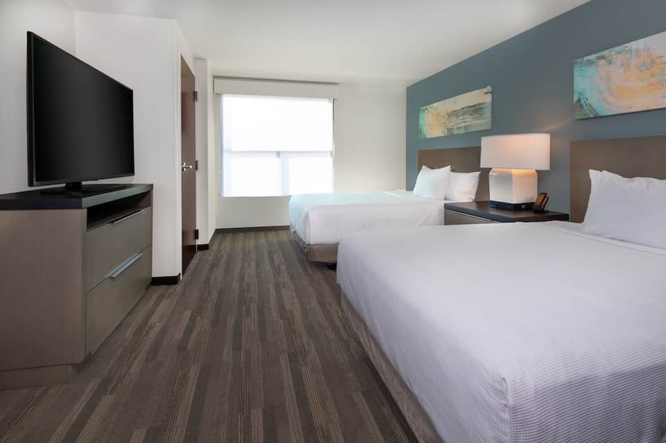 Modern hotel guest room with two queen beds, blue accent wall, and flat-screen TV