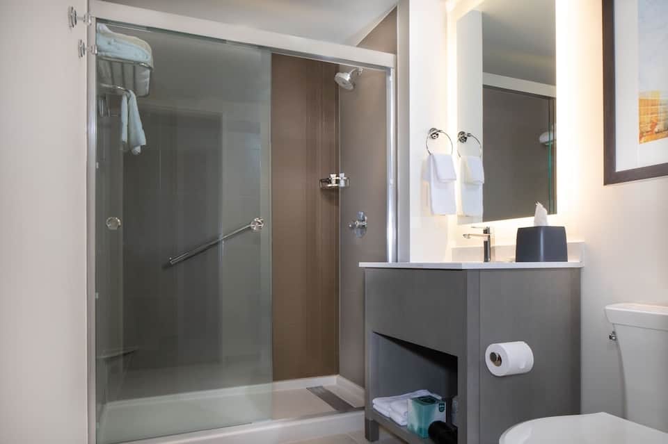 Modern bathroom with glass shower enclosure, gray vanity with white sink, white towels, and contemporary fixtures.