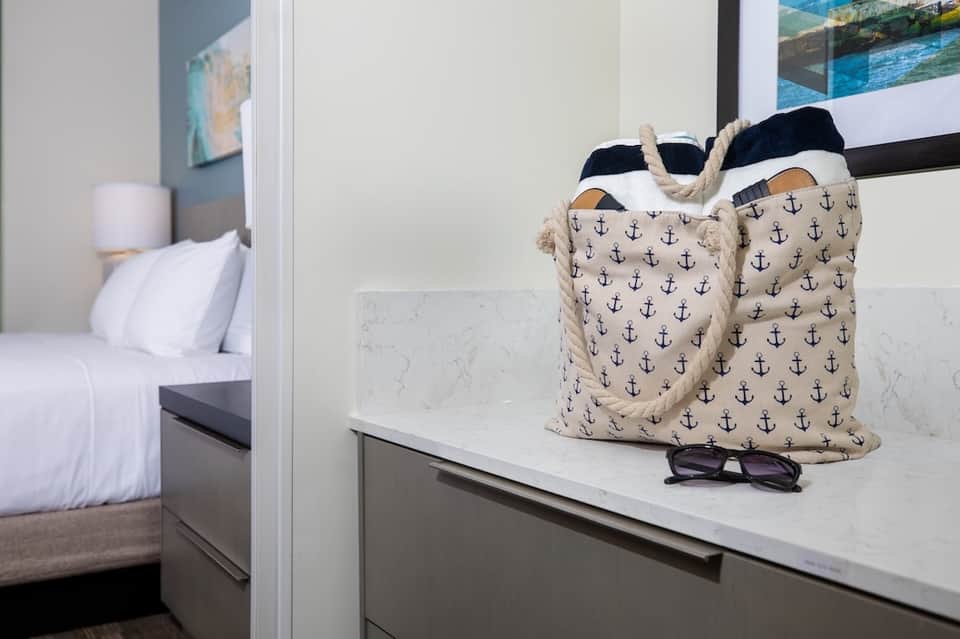 Bathroom vanity with anchor-patterned tote bag and sunglasses, bedroom visible through glass door