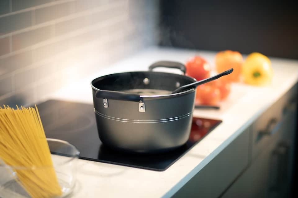 Kitchen stovetop with black cookware, pasta, and fresh vegetables in bright natural light