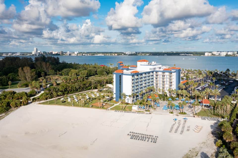 Beachfront resort with blue and orange building, sandy beach, palm trees, and bay view