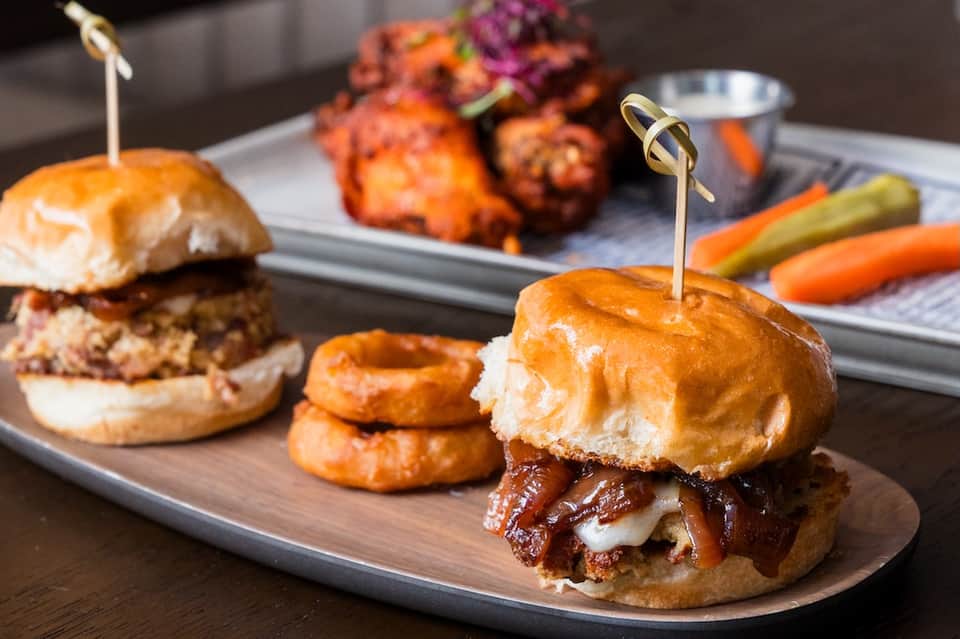 Gourmet appetizers including sliders, fried appetizers, onion rings, and pickles on white serving platters
