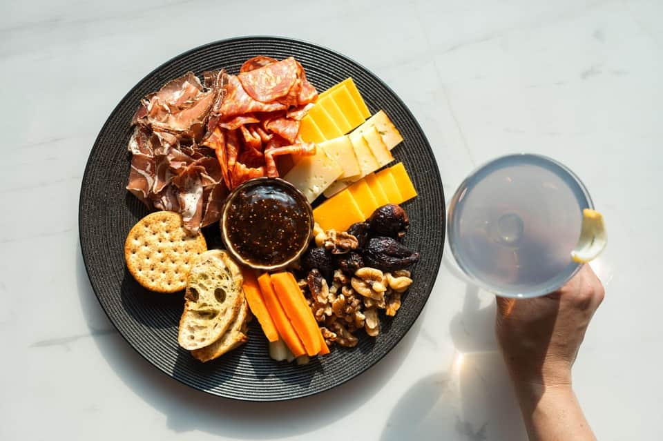 Charcuterie board with cured meats, cheese, crackers, nuts, and dip with beverage