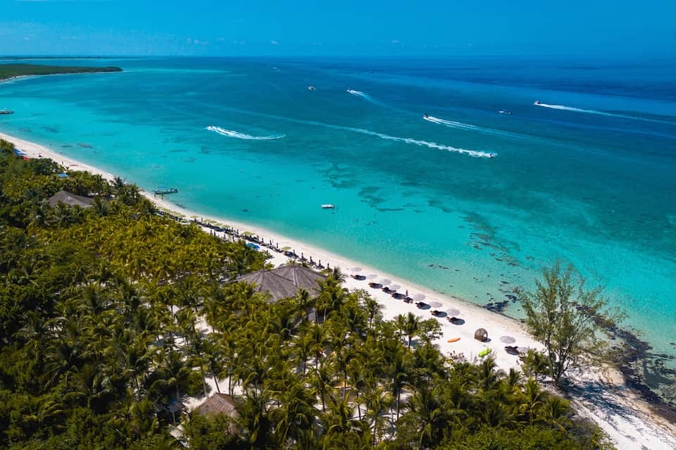 Aerial beach resort view with turquoise waters, white sand, palm trees, and ocean waves