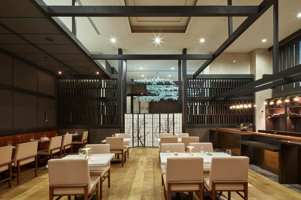 Modern fine dining restaurant with dark wooden beams, cream chairs, and illuminated bar