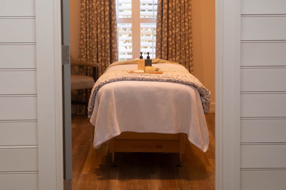 Spa treatment room with massage table, warm orange walls, flowing curtains, and spa amenities