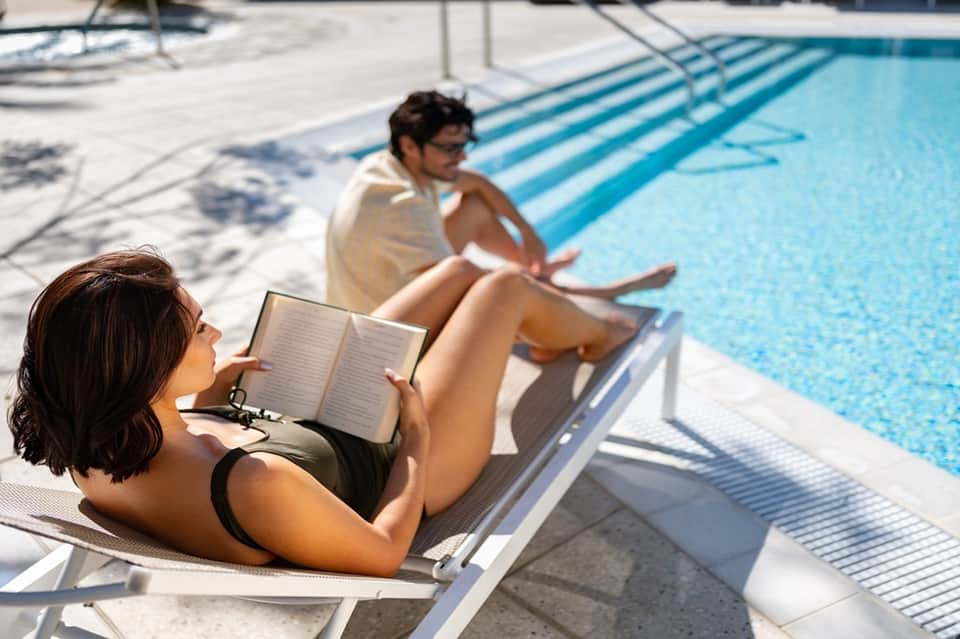 Guests relaxing poolside, one reading by the water with clear blue lap pool visible