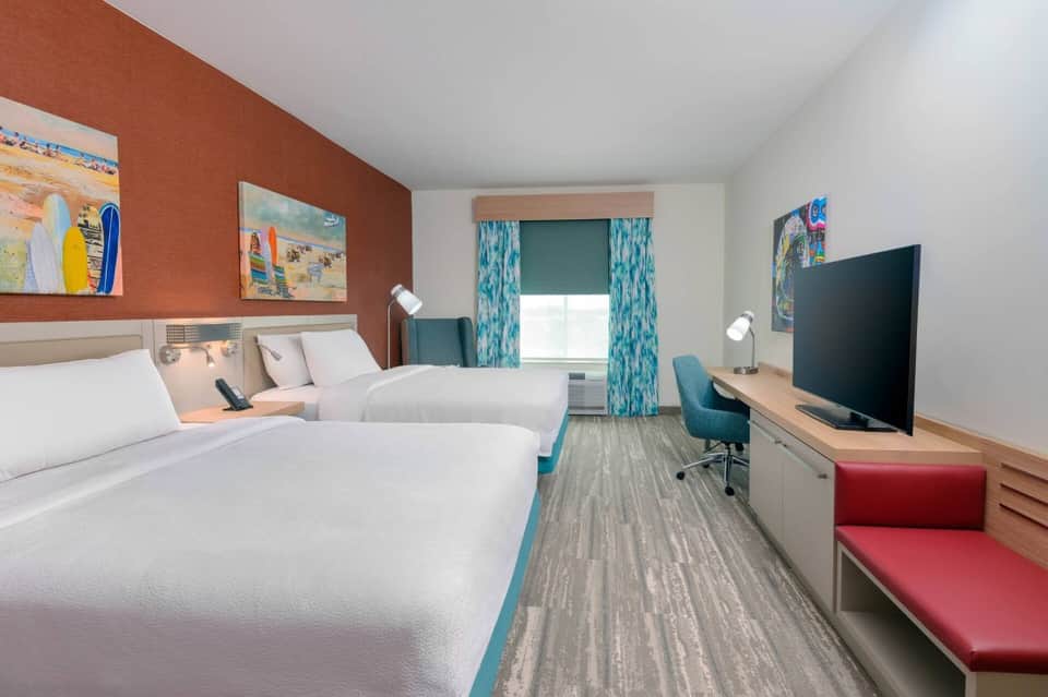 Hotel guest room with two queen beds, orange accent wall, and beachy decor
