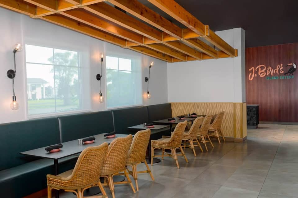 Modern restaurant interior with teal banquette seating, rattan chairs, wooden beam ceiling, and contemporary lighting