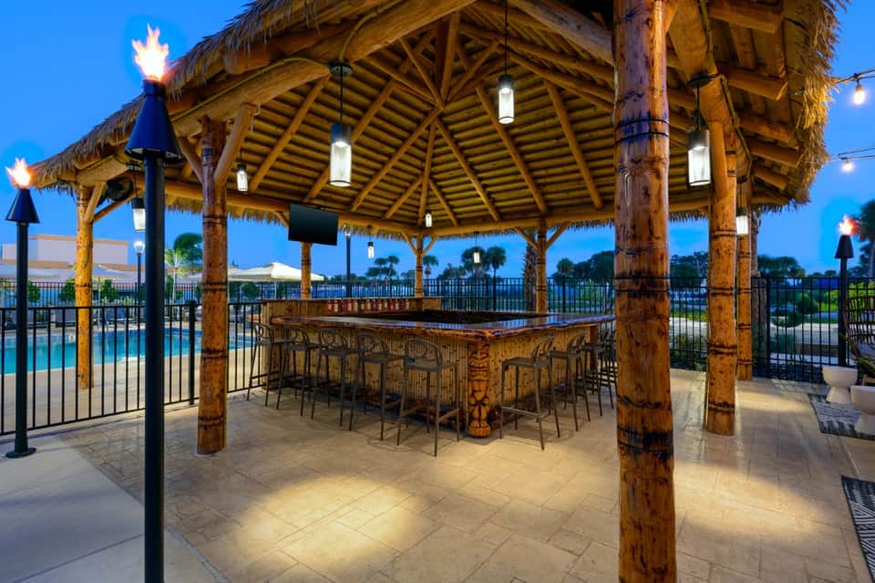 Tiki-style bar pavilion with wooden beams overlooking pool and grounds at dusk