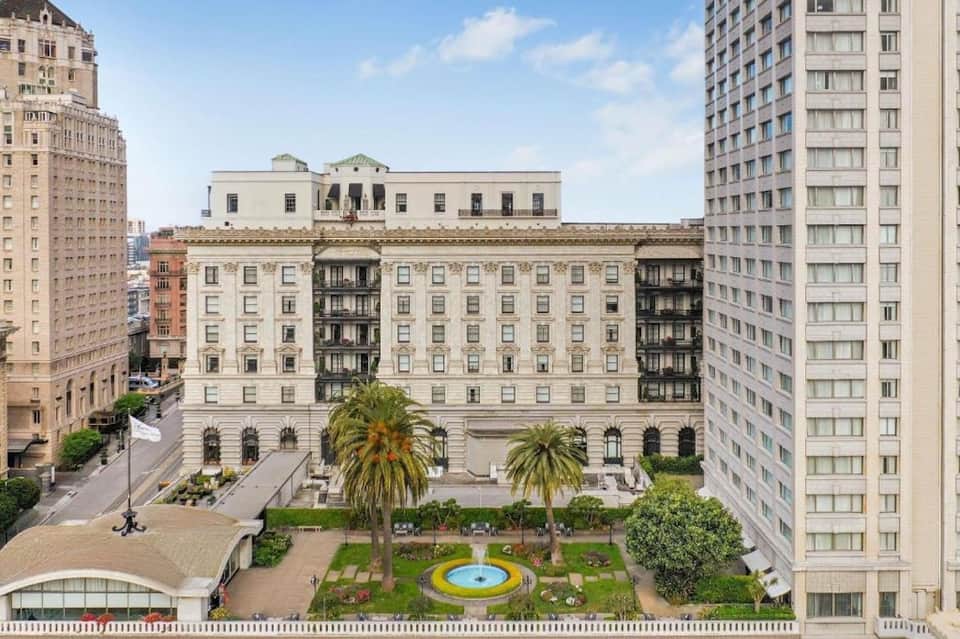 Historic beaux-arts hotel building with ornate facade, palm trees, and urban plaza setting
