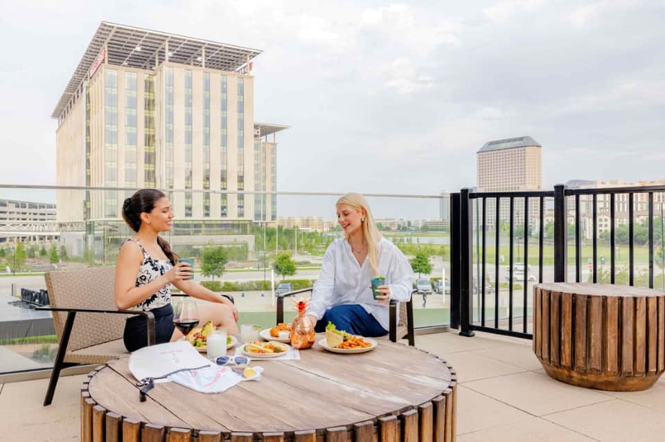 Two women dining on rooftop terrace with city skyline and river views in background