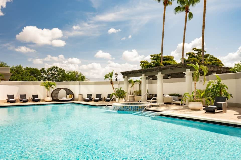 Luxury resort pool with turquoise water, palm trees, lounge chairs, and white pergola