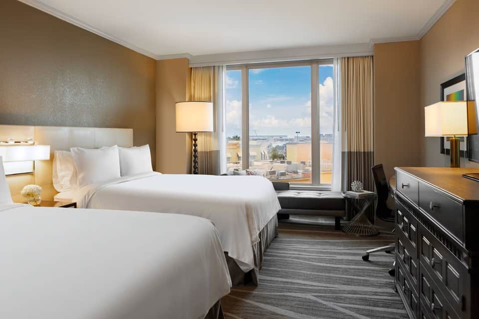 Hotel bedroom with two queen beds, warm tones, city views from large windows