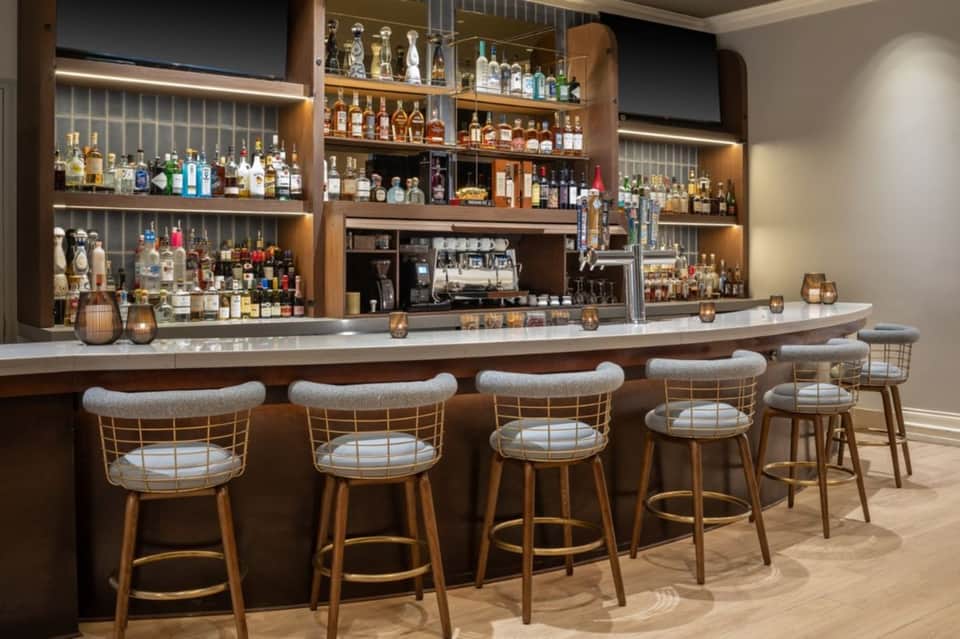 Elegant hotel bar with wood cabinetry, extensive liquor selection, and upholstered bar stools