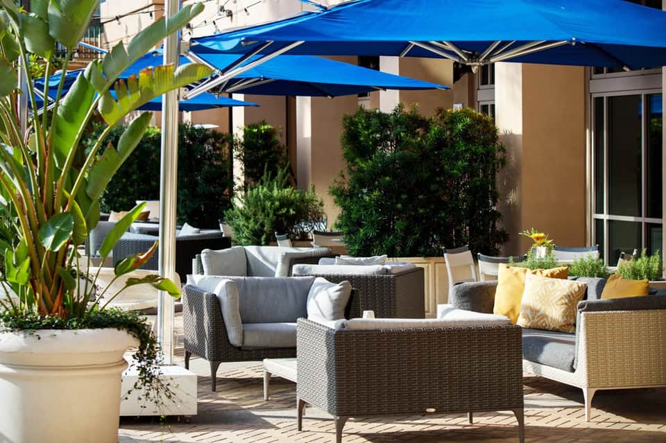 Outdoor terrace with wicker lounge chairs, blue umbrellas, and tropical plants