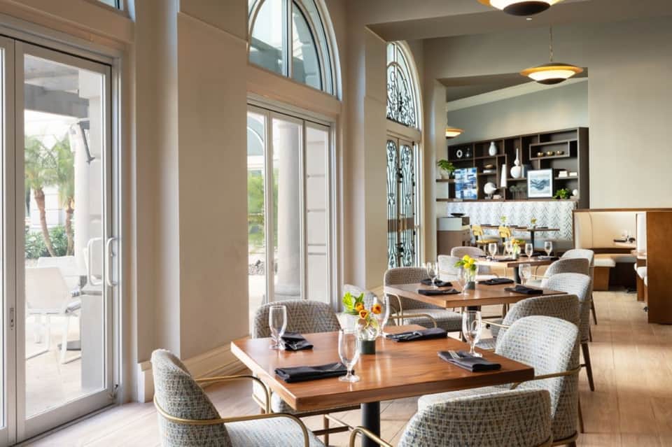 Upscale hotel dining room with wooden tables, wicker chairs, and open doors to patio