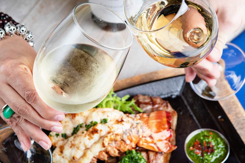 Two wine glasses toasting over grilled lobster and fresh salad at an outdoor dining table