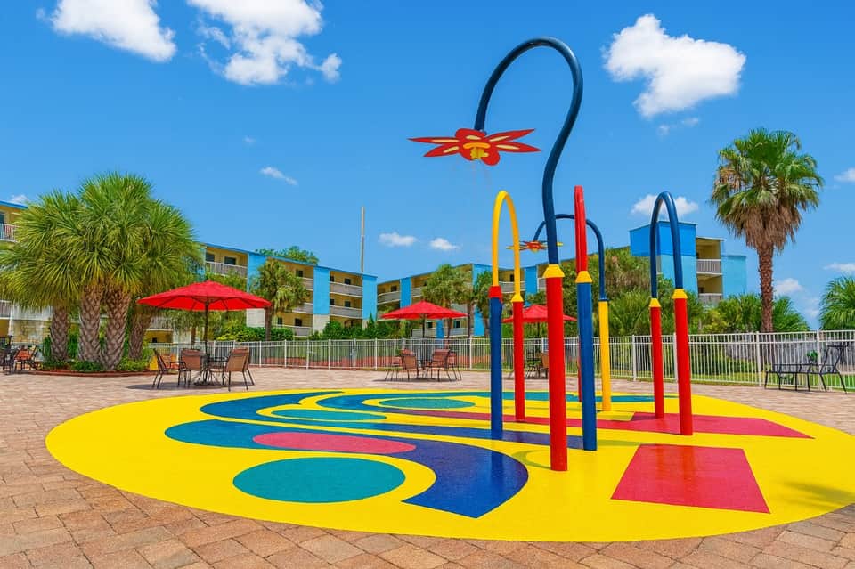 Colorful splash pad with yellow and blue play surface, rainbow arch, and red umbrella