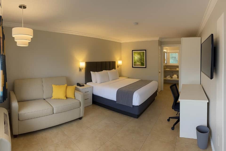 Spacious hotel room with queen bed, sofa, work desk, and bathroom visible