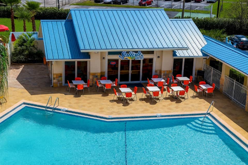 Outdoor pool with blue metal roof Splash Bar, red chairs, and palm landscaping